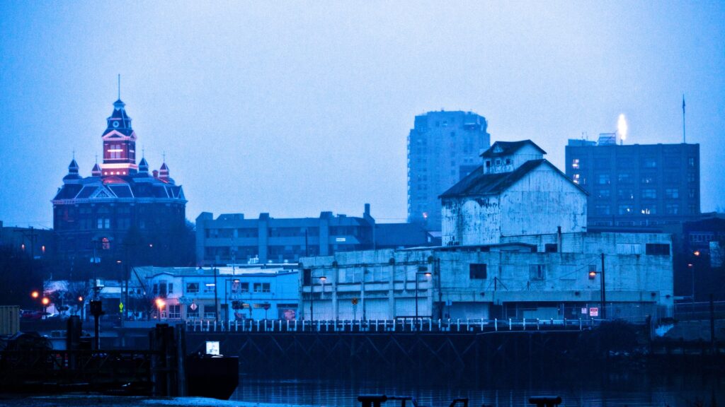 Foggy cityscape with a historic building featuring a red-lit dome, seamlessly blending into the commercial real estate landscape, surrounded by modern and older structures against a misty blue sky.