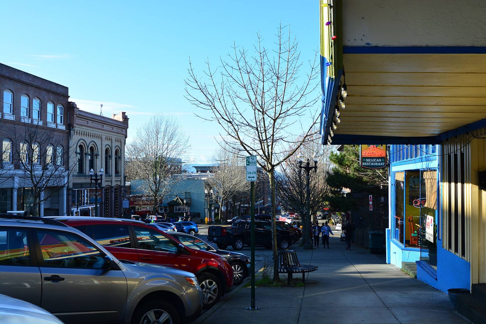 Sidewalk under a shop awning in Fairhaven with brick buildings and parked cars along the street