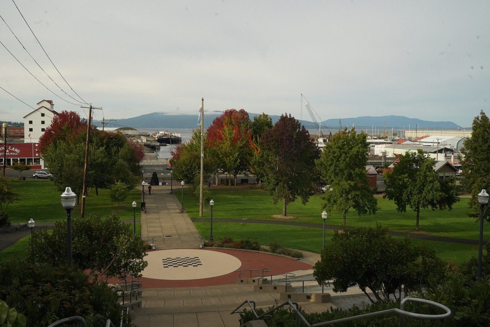 Lawn and paths of Maritime Heritage Park seen from the top of the amphitheater, with the waterfront and hills beyond