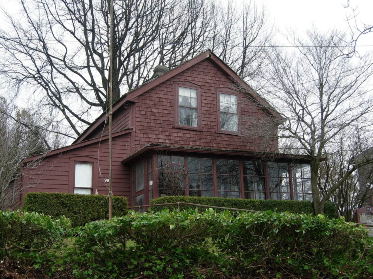 Two-story reddish wood house with an enclosed porch behind a trimmed hedge, the Pickett House