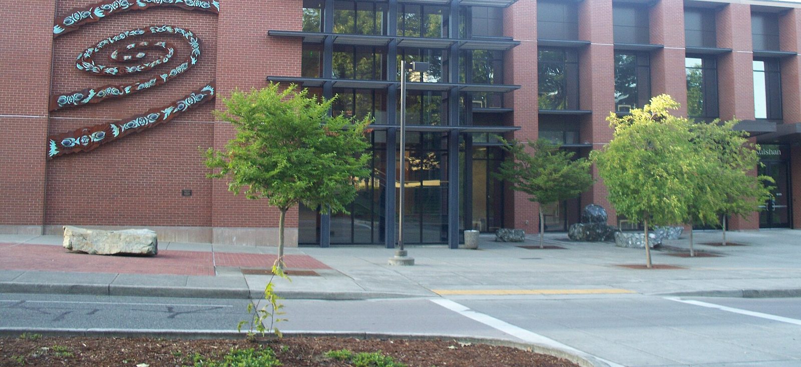 Brick and glass Kulshan Hall at Whatcom Community College with young trees and a walkway in front